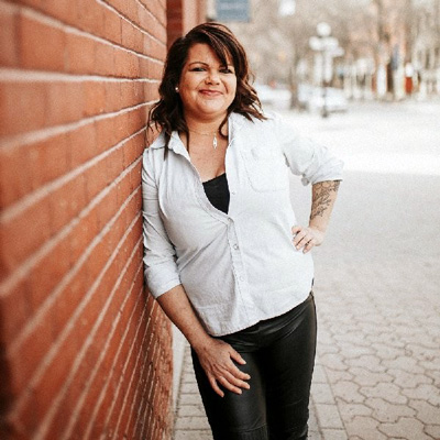 Photo of Michelle Virog leaning on a brick wall smiling